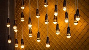 Vários bulbos de iluminação, pendurados pelos fios, iluminam uma parede decorada ao fundo.