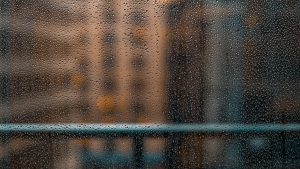Gotas de água se acumulam em vidraça com prédios desfocados ao fundo