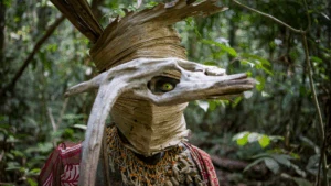 Masque rituel en fibres végétales avec un grand œil peint, au milieu de la forêt