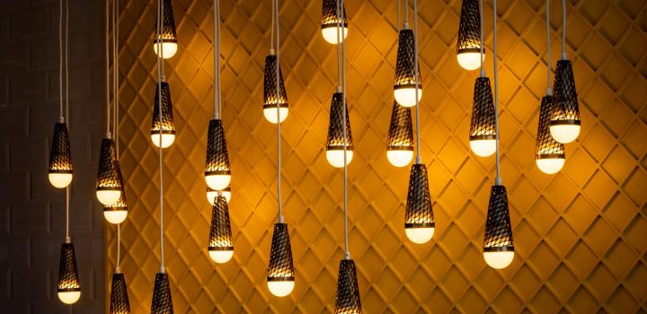 Vários bulbos de iluminação, pendurados pelos fios, iluminam uma parede decorada ao fundo. Saiba como proteger obras de arte de luzes inadequadas.